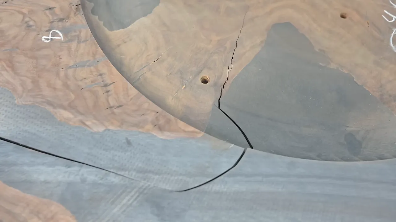 Large crack running through gray epoxy in a round wood tabletop