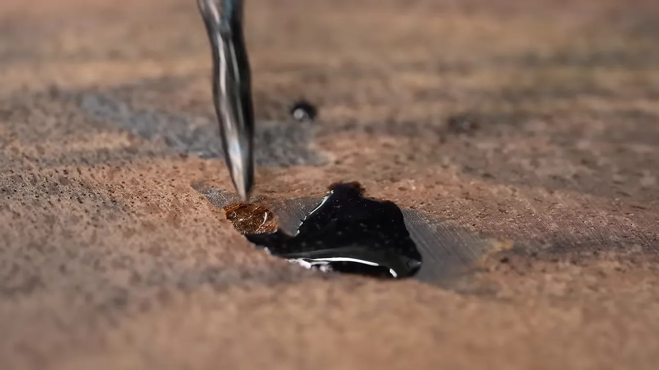 Metal point working black epoxy into a small hole in the wood surface