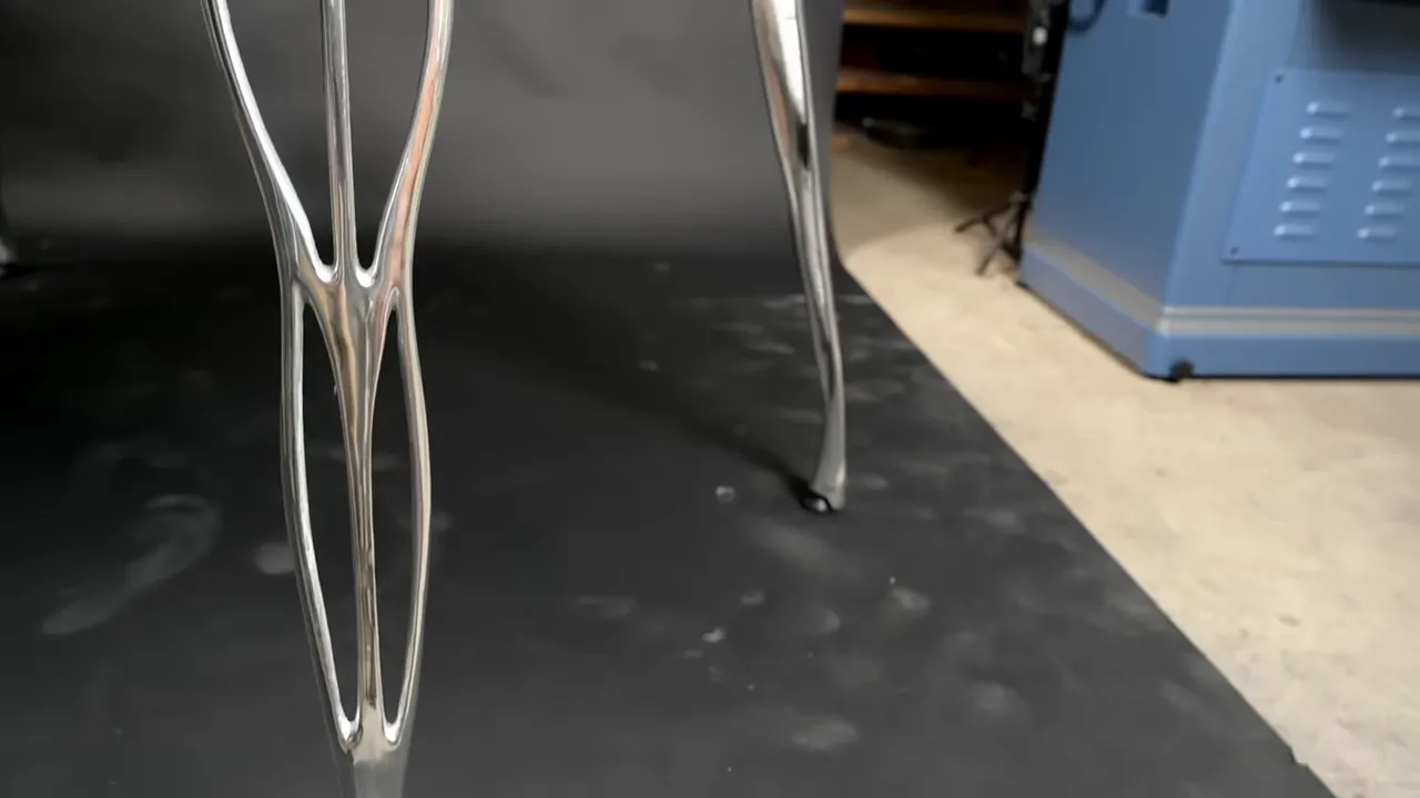 Polished aluminum table legs with elongated open shapes standing on a dark floor