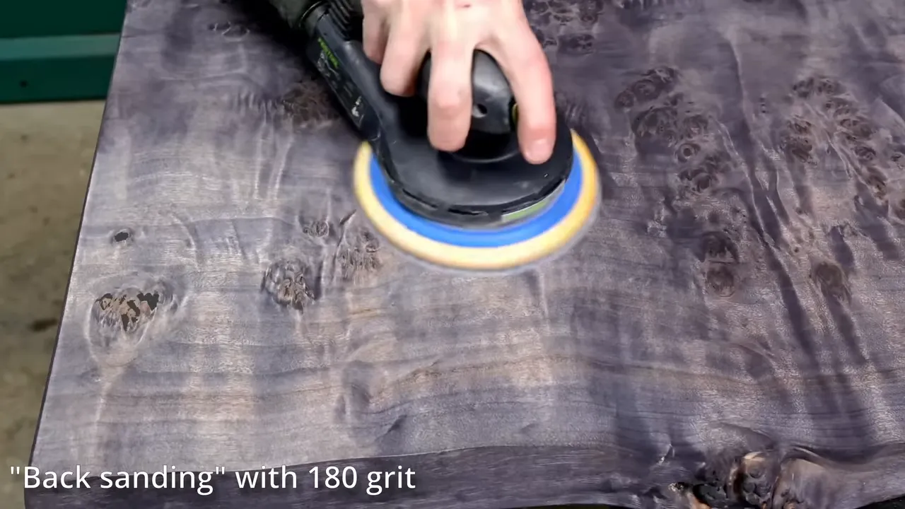 Random orbital sander moving across a gray-black dyed burl surface with contrasting figure