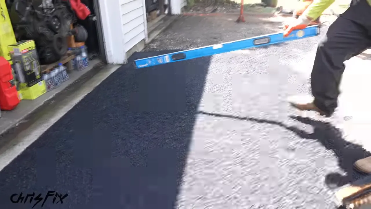 Worker checking fresh asphalt at the garage entrance with a blue level