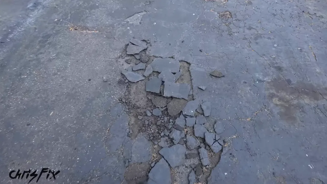 Broken asphalt pieces surrounding a large depression in the old driveway