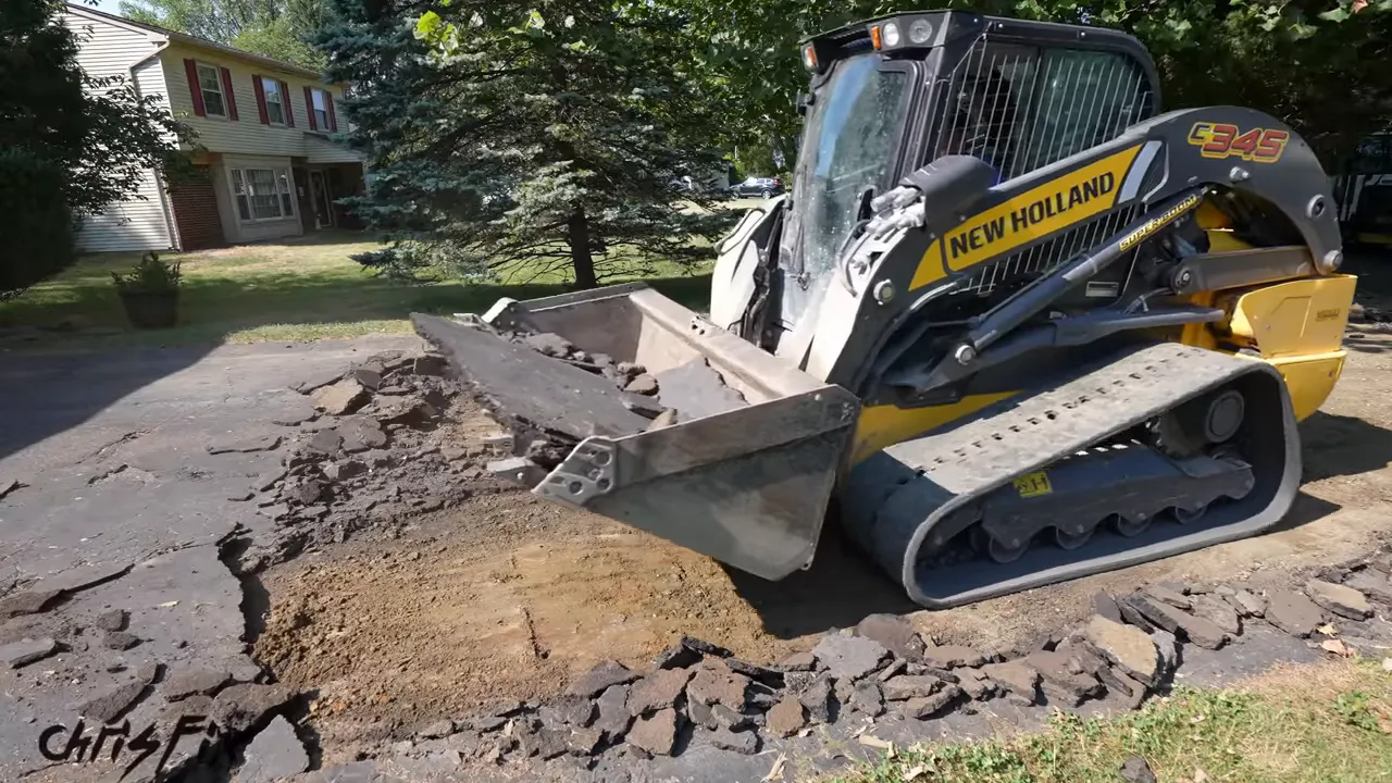 Skid steer lifting old asphalt beside an exposed strip of compacted ground