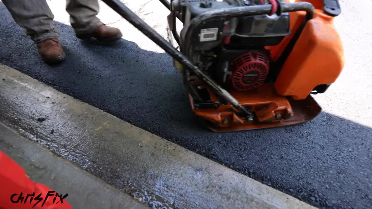 Plate compactor finishing fresh asphalt beside the concrete garage threshold