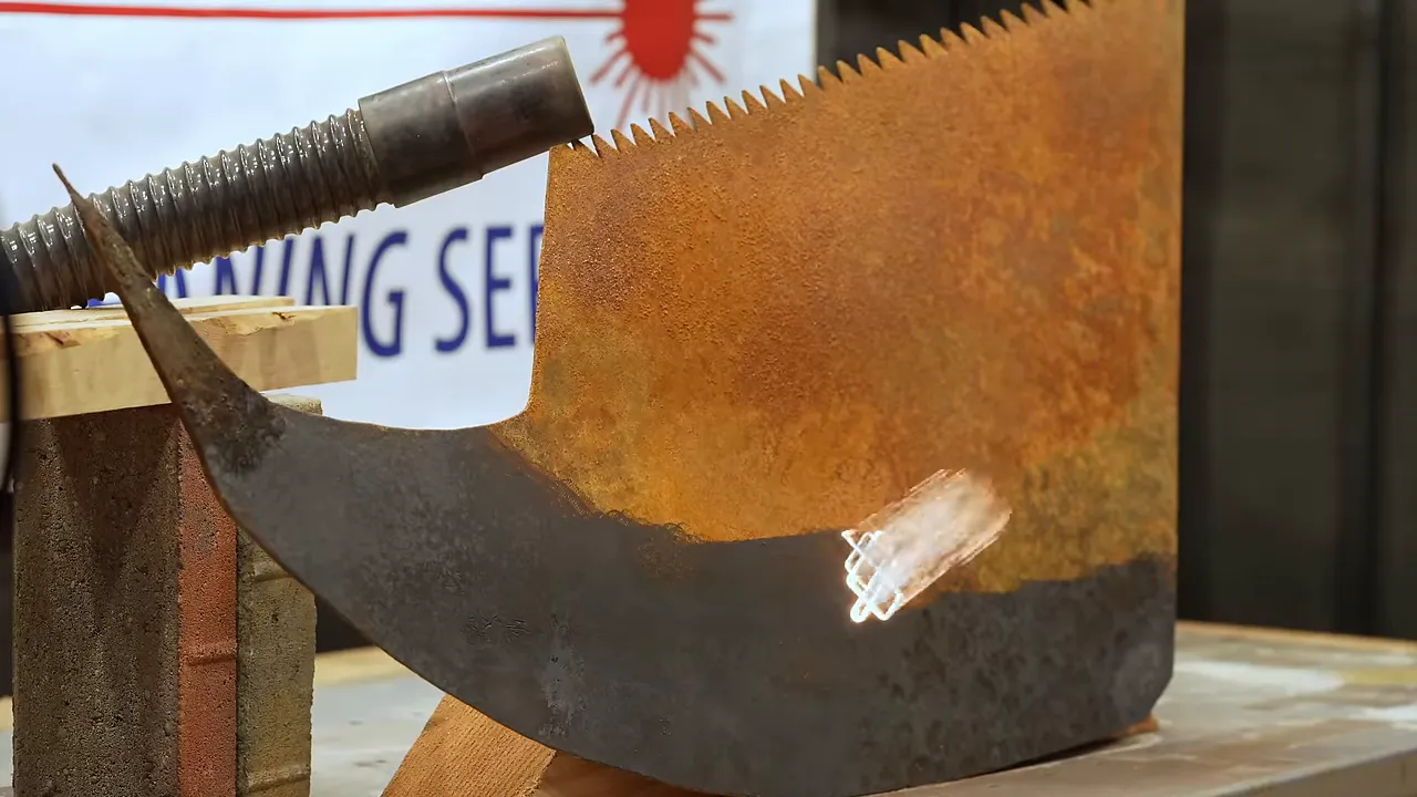 Laser cleaning a broad saw blade with orange rust above a dark cleaned strip