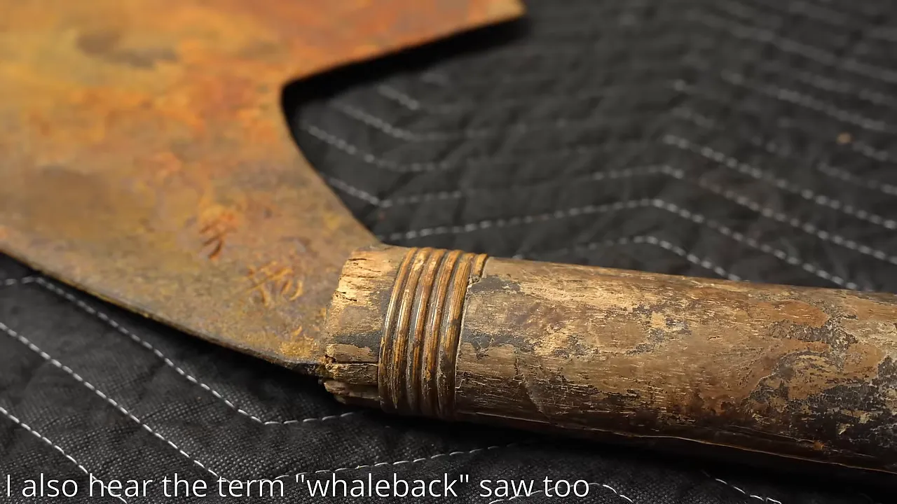 Worn wooden handle and rusty saw blade resting on a black moving blanket
