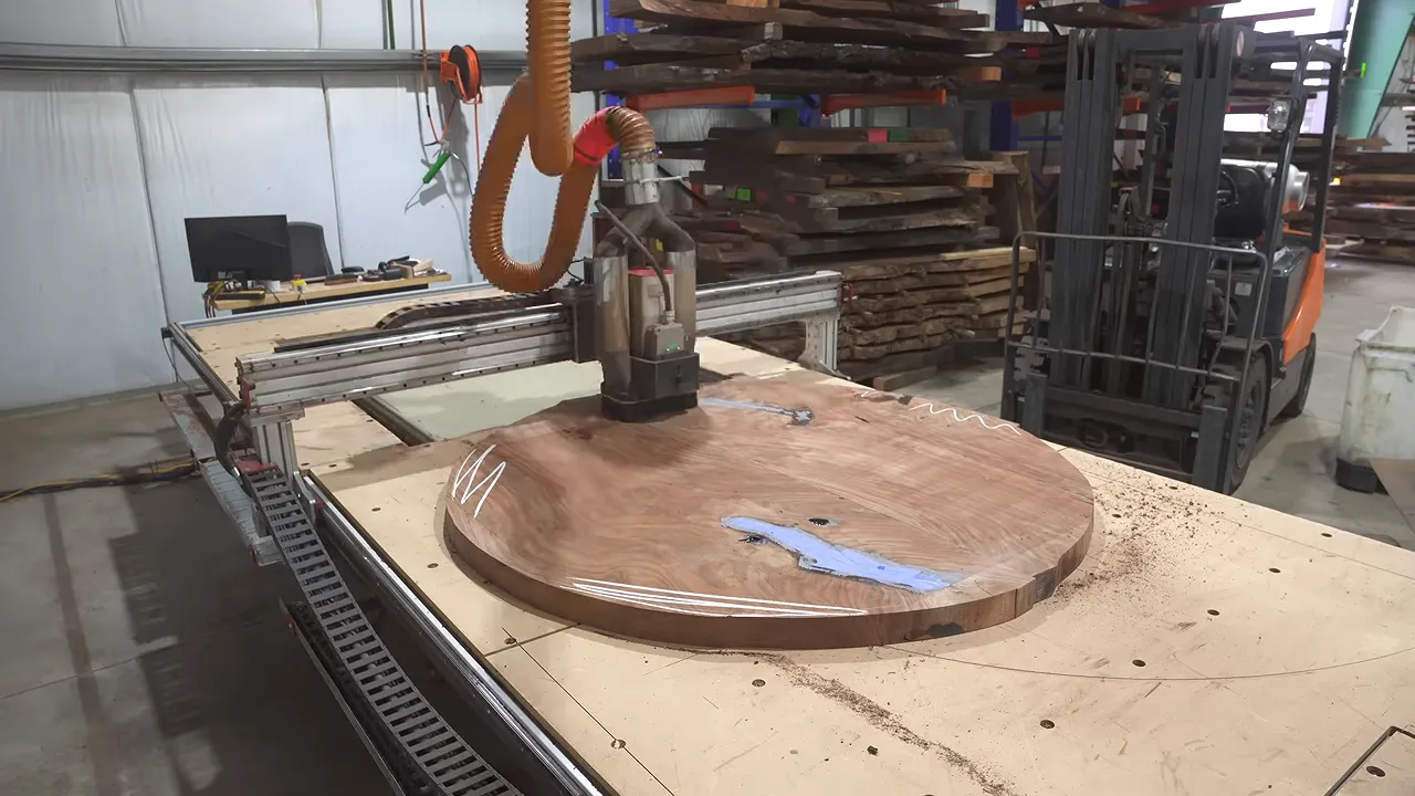 Large circular walnut tabletop on a CNC bed beneath a router spindle