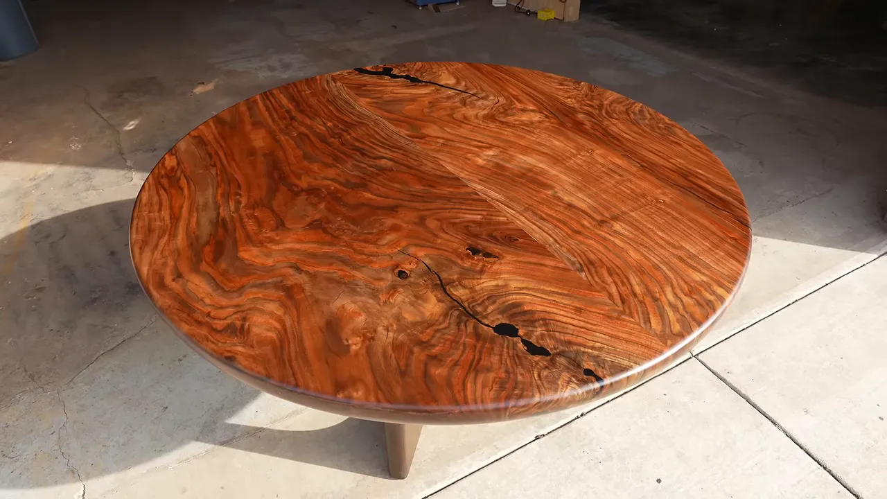Finished round walnut table with figured grain and opposing dark epoxy-filled cracks