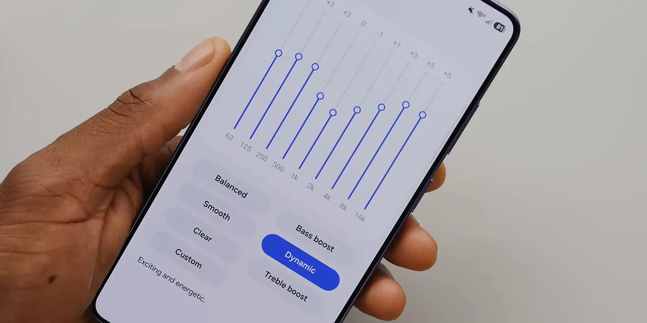 A hand holding a phone displaying nine equalizer sliders and sound presets