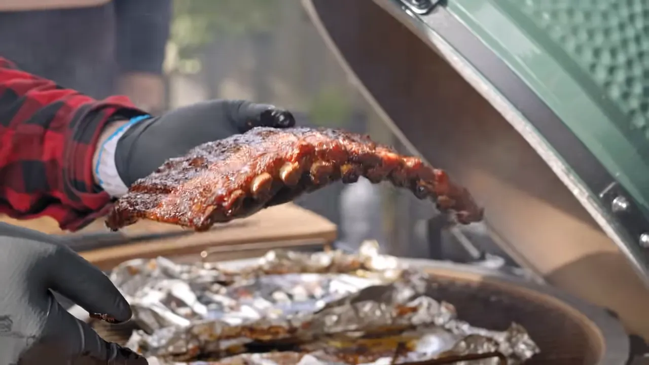 A cooked rib rack bending while held above foil boats in the open grill
