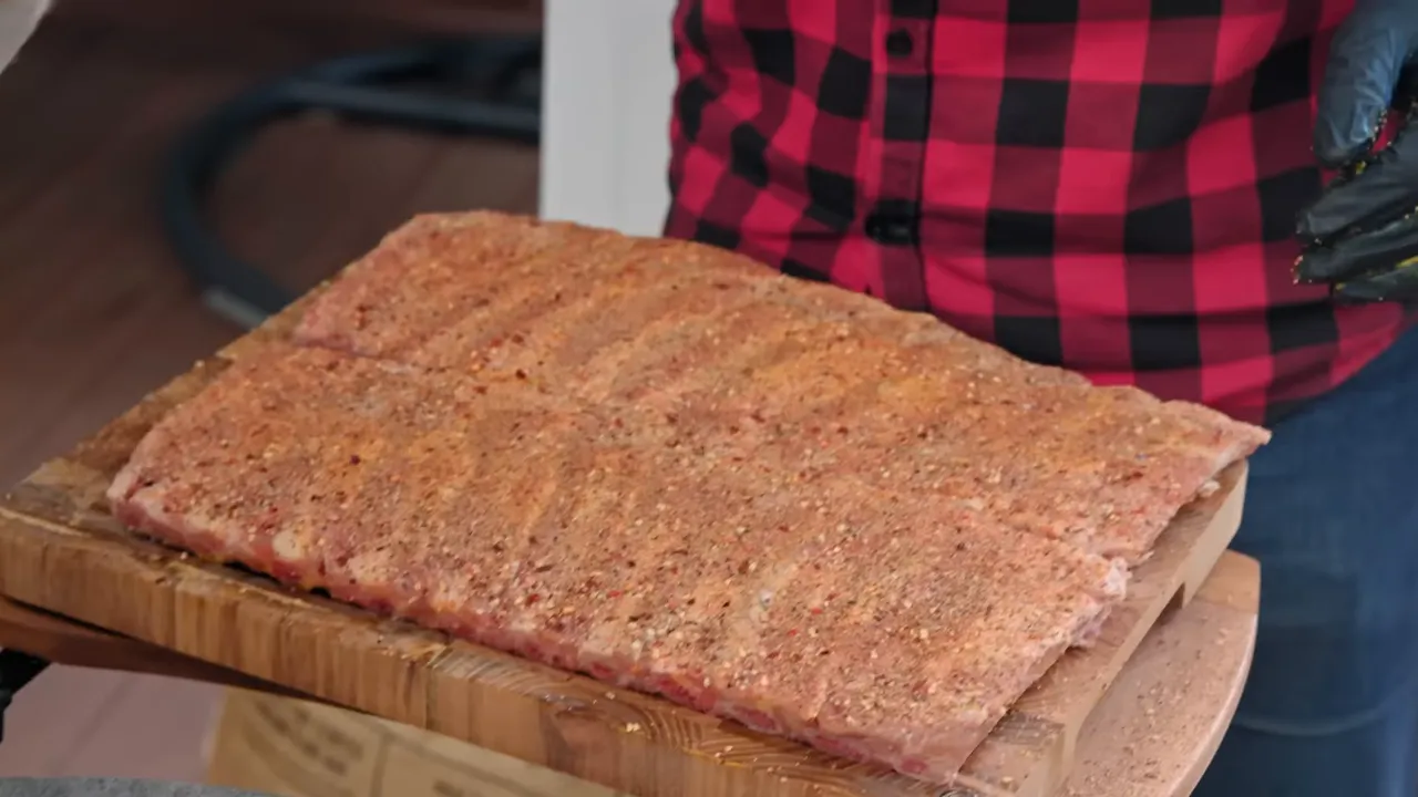 Two raw rib racks evenly coated with dry seasoning on a wooden board