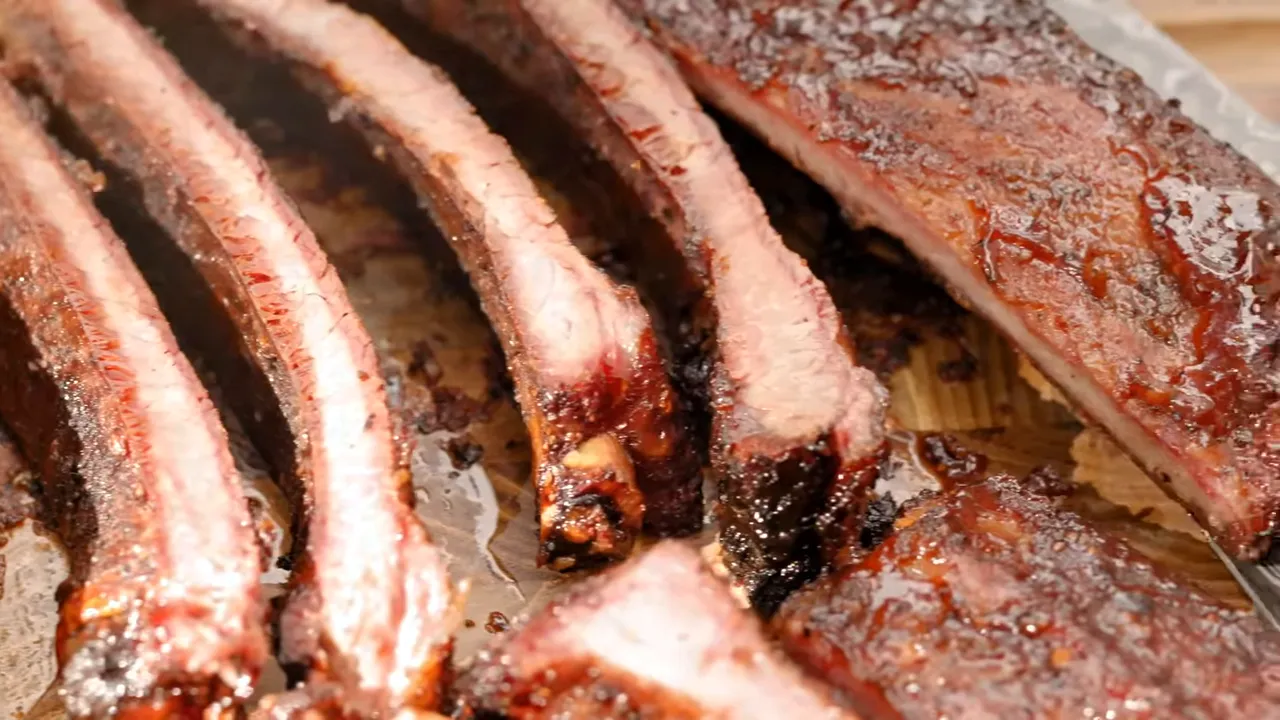 Sliced ribs showing pink edges beneath dark bark on a wooden board