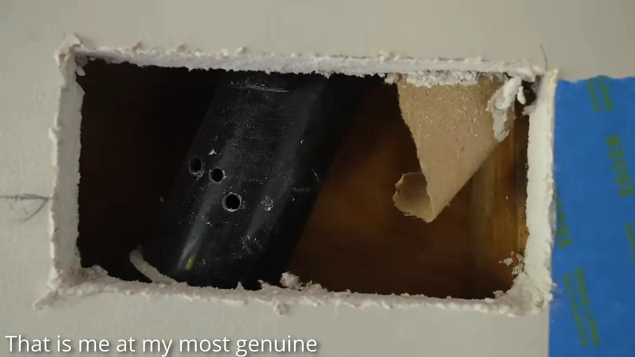 Black pipe with several drilled holes visible through a rectangular drywall opening