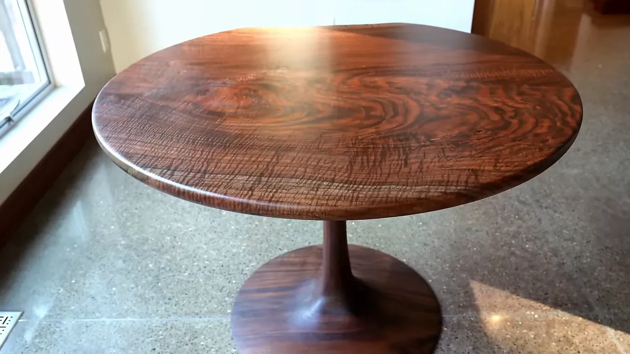 Completed round walnut table with a sculpted pedestal beside a window