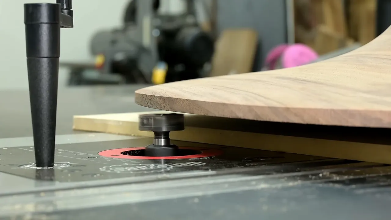 Walnut pedestal foot rotating above a router-table cutter beside the jig support