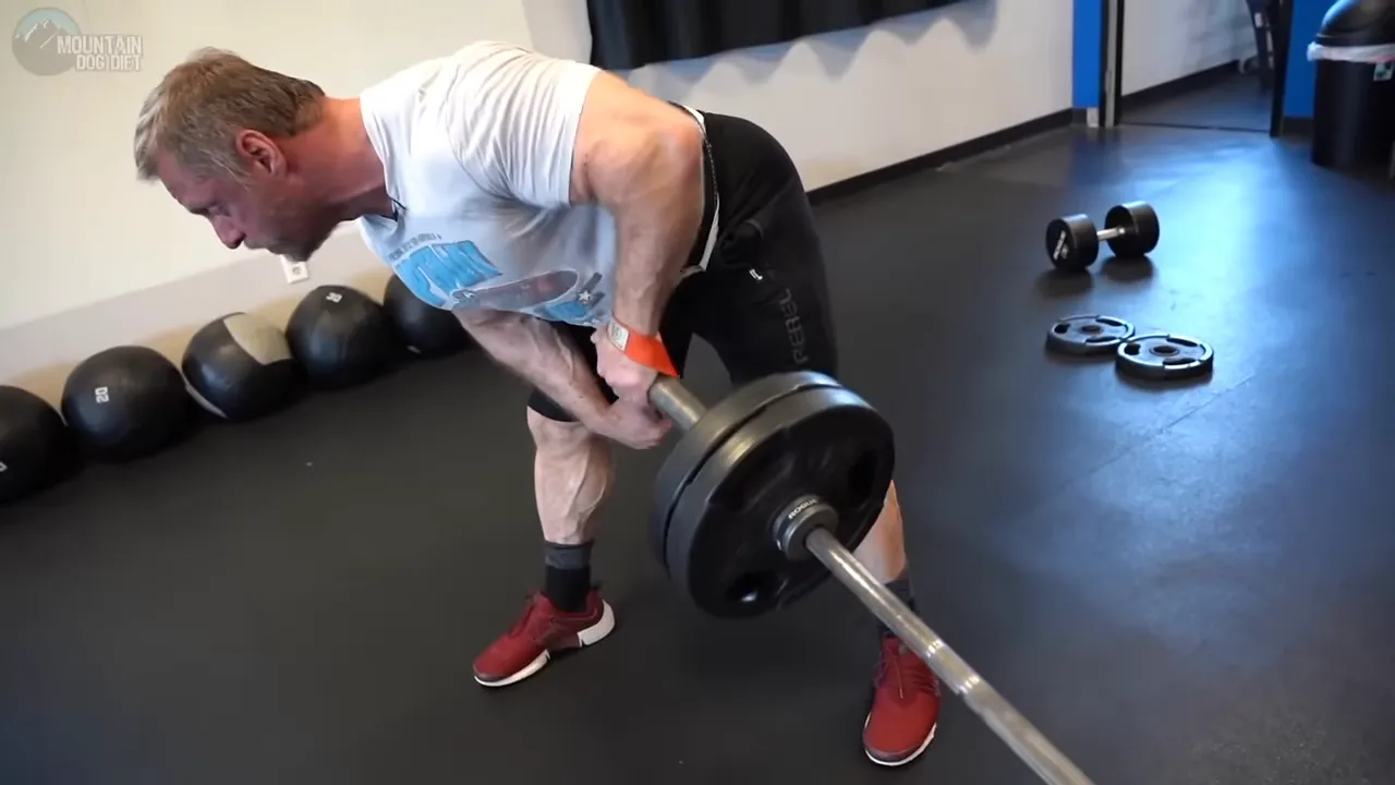John Meadows rowing the loaded end of a barbell with his other arm braced against his thigh