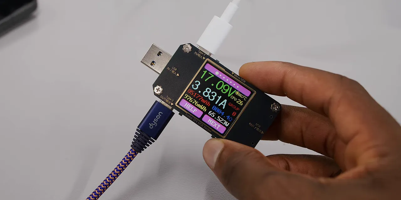 Hand holding a USB power meter connected between two charging cables