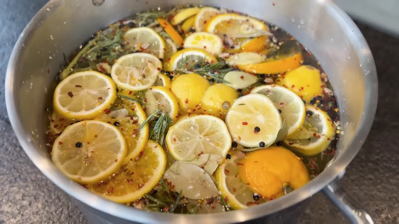Pot of brine containing sliced citrus, herbs, ginger, and peppercorns