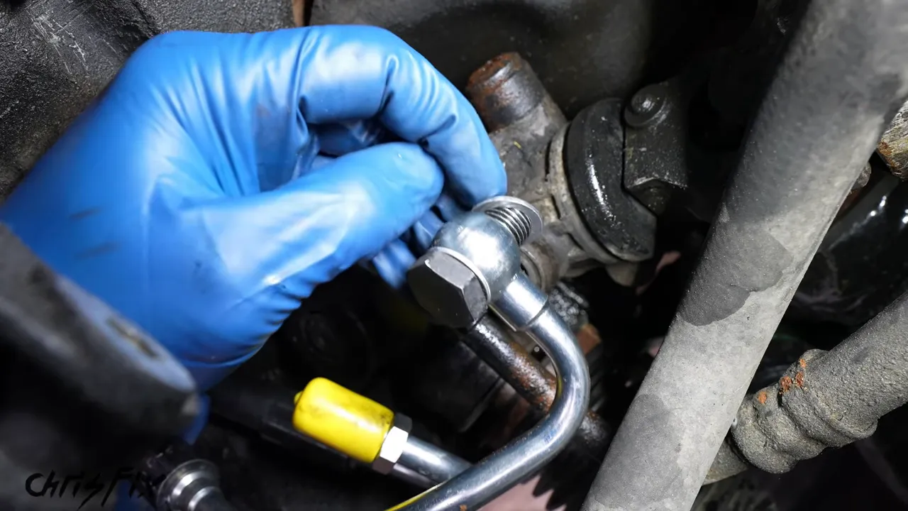 Gloved hand holding the banjo bolt and pressure-line fitting with a silver crush washer visible behind the fitting