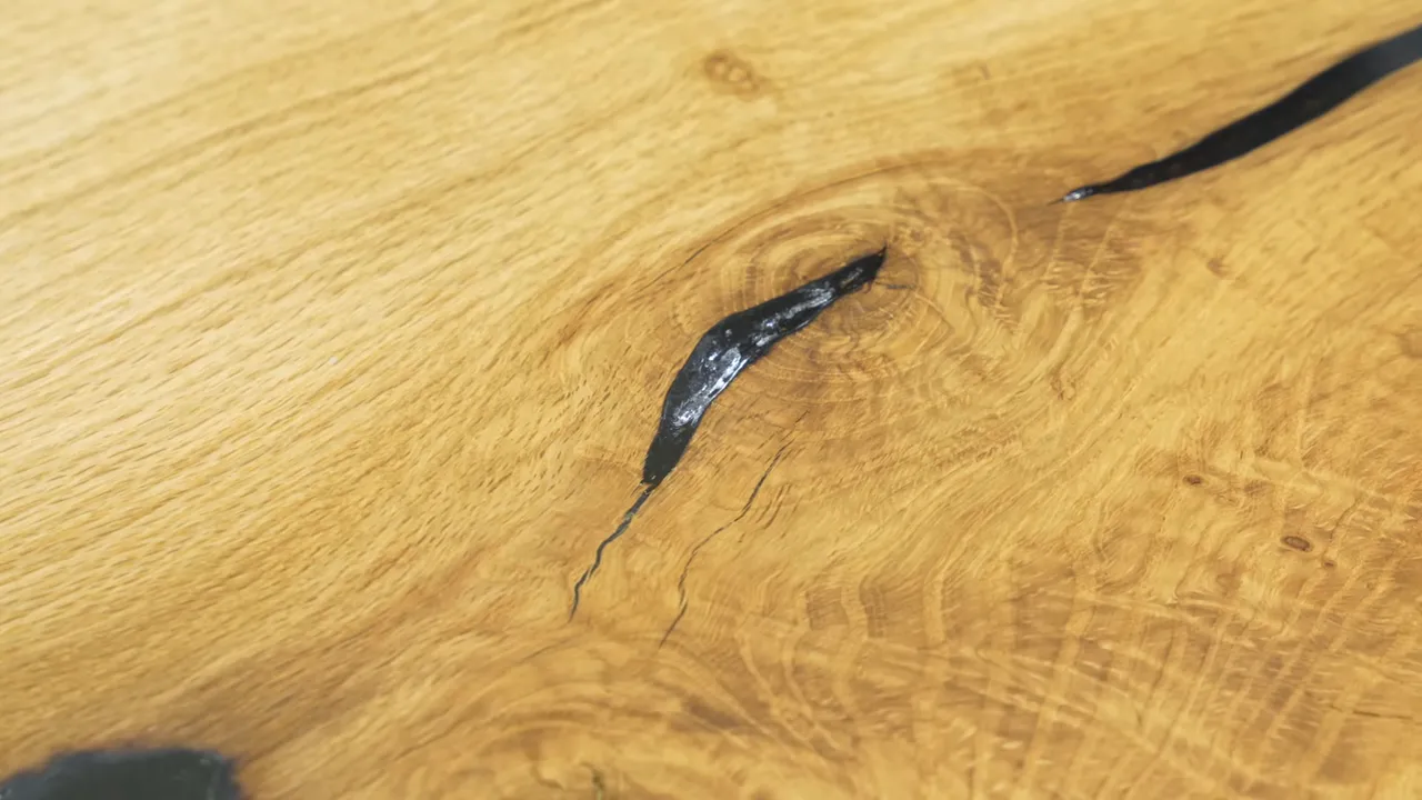 A close-up of a narrow epoxy-filled oak crack with a pale reflective area along its edge
