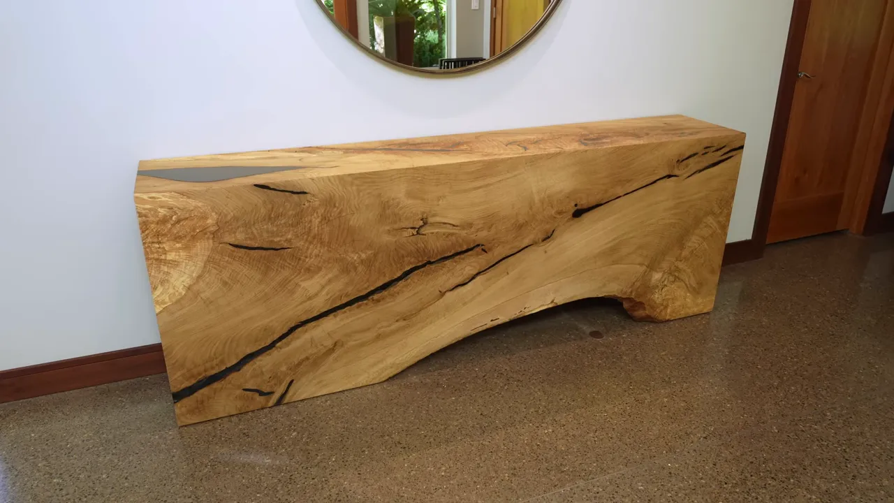 The finished oak waterfall console against a white wall beneath a round mirror