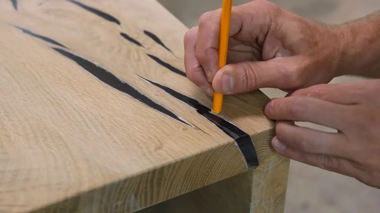 A pencil-shaped sanding tool working along the boundary between pale oak and dark polished epoxy