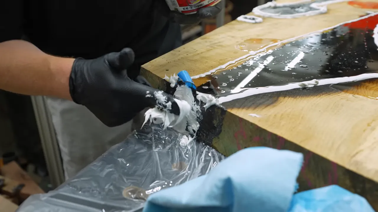 Gloved hands pressing gray sealing paste against an epoxy leak at the slab edge