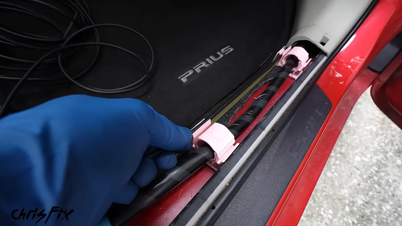 Rear camera cable routed beside a washer hose in clips along the exposed door sill