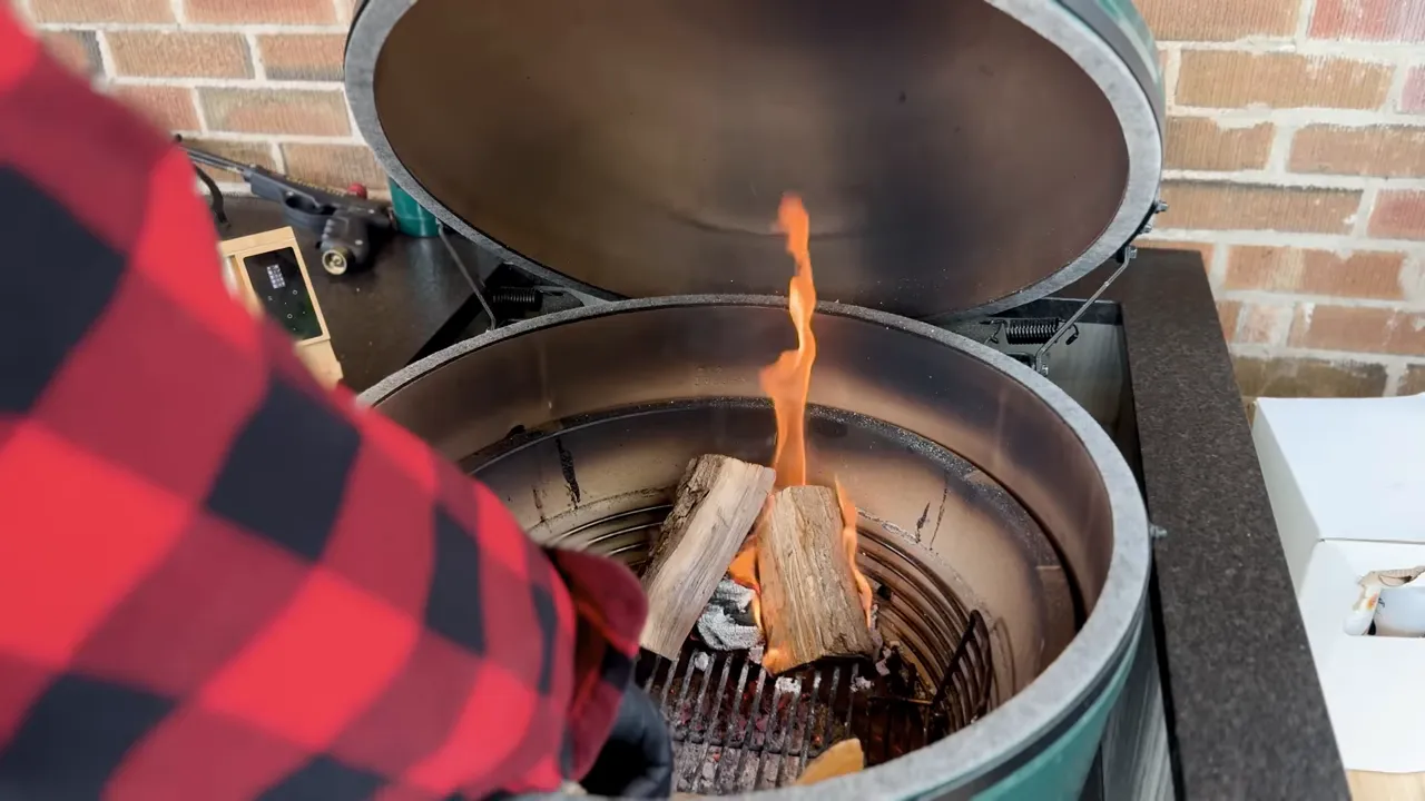 Wood splits burning with visible flames in a charcoal basket inside an open Big Green Egg