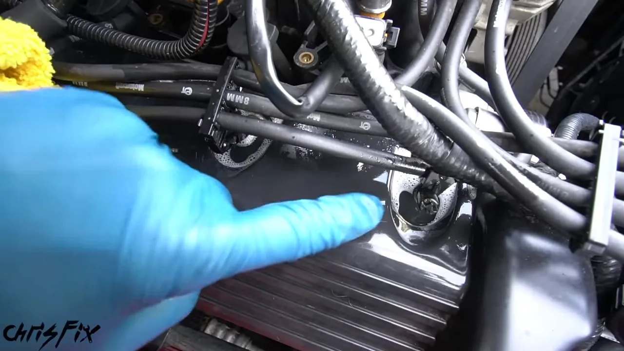 Gloved finger indicating pooled water around a spark plug boot on the engine