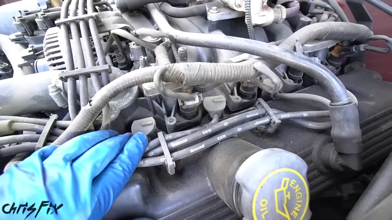 Gloved hand pointing toward spark plug boots and recessed areas on top of the engine