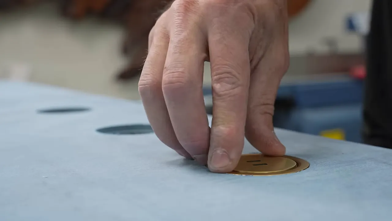A round brass outlet fitting sitting flush in the pale blue denim desktop