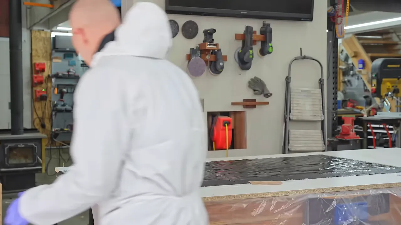 Gloved hands pressing a squeegee across an epoxy-soaked denim sheet on a flat form