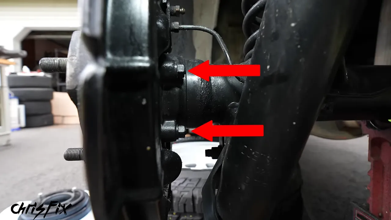 Two axle retaining nuts behind the brake backing plate marked with red arrows