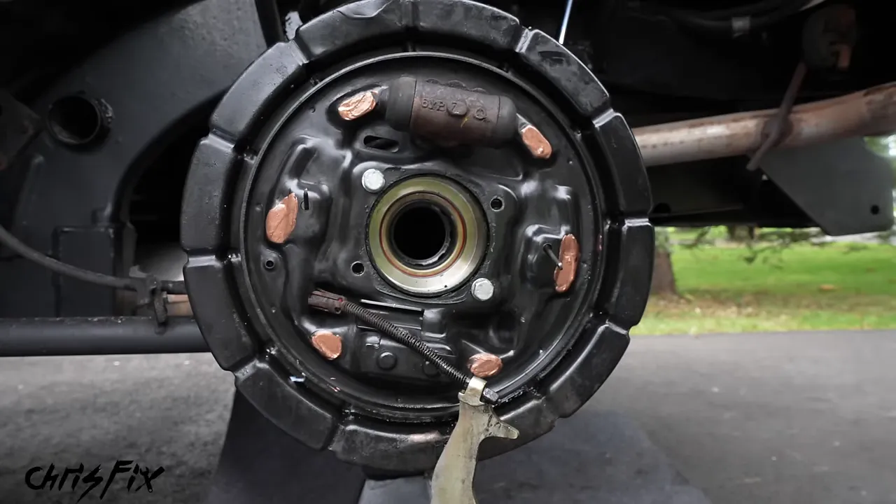 Cleaned drum brake backing plate with copper-colored lubricant on six shoe contact points