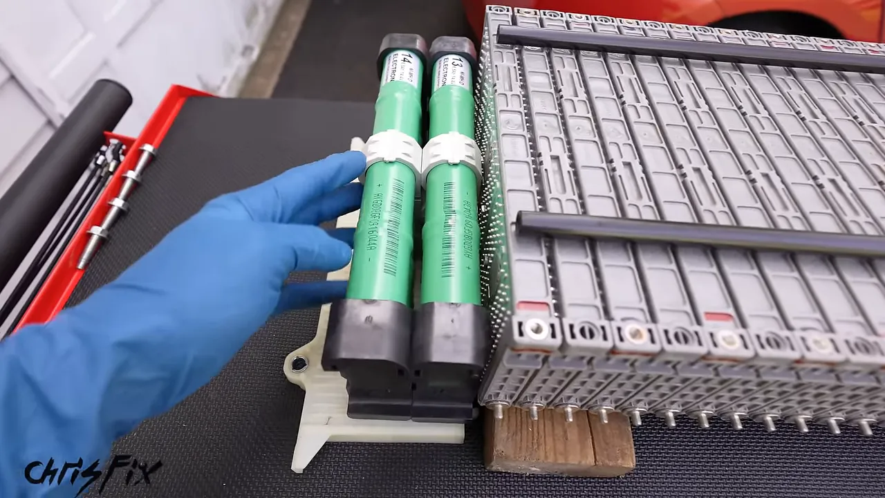 Green cylindrical battery assembly held beside the original gray prismatic battery modules