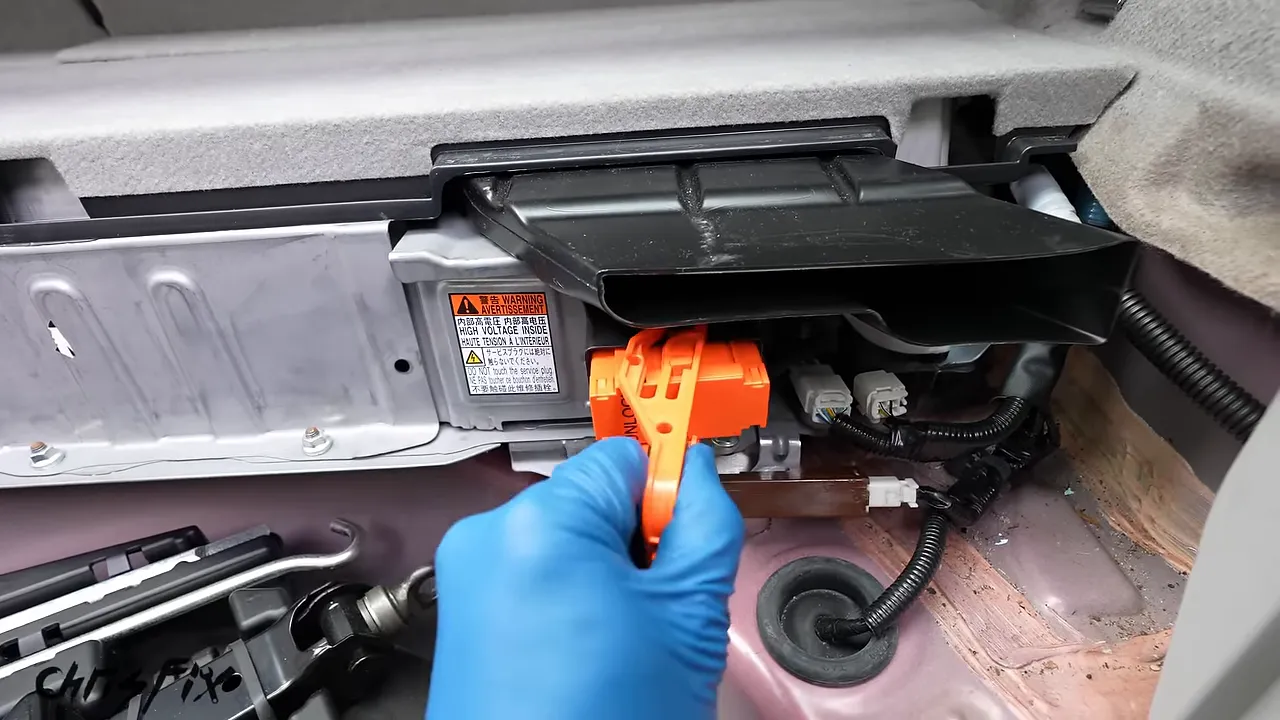 Orange hybrid battery service plug being withdrawn from its socket in the cargo area