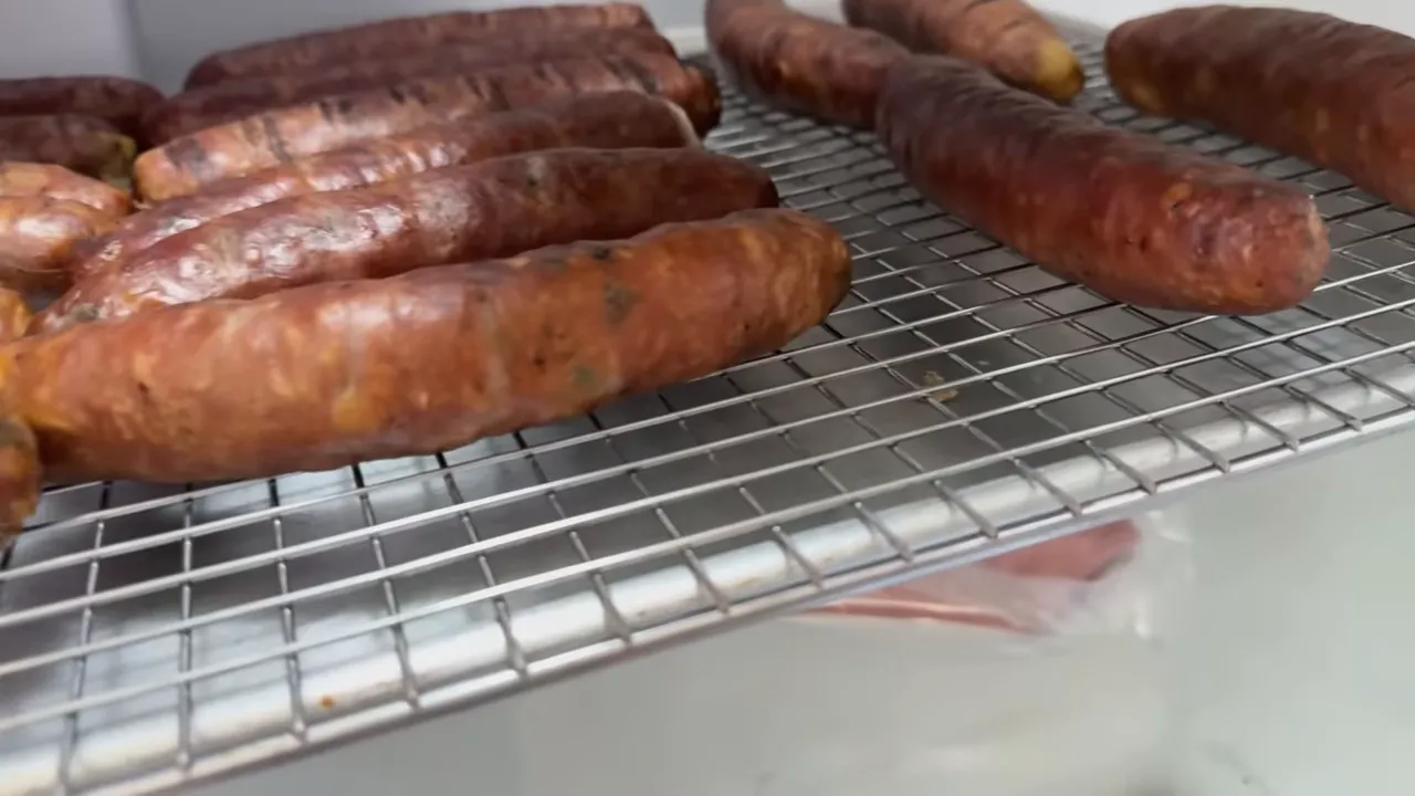 Smoked sausages spaced on a wire rack over a tray inside a refrigerator