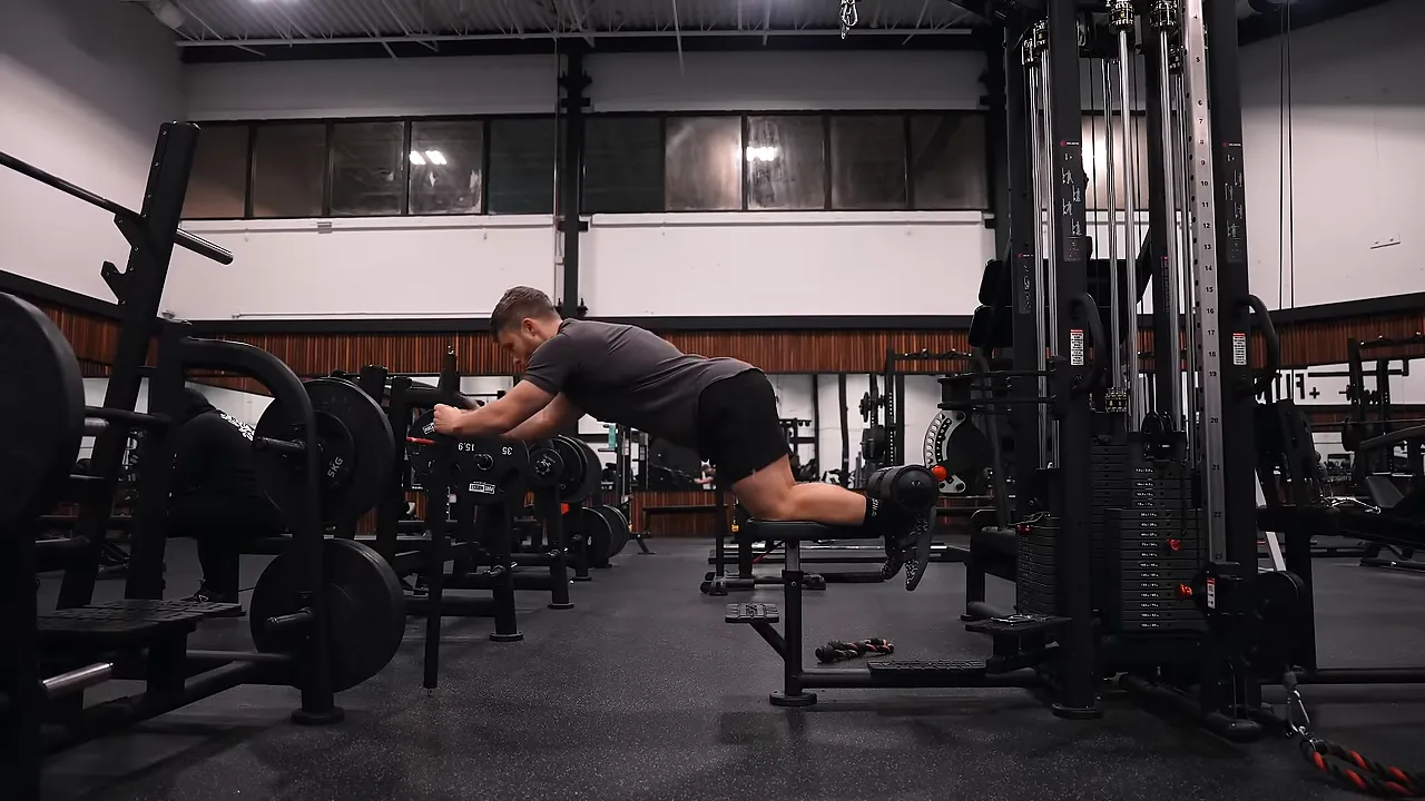 Glute-ham raise variation on a lat pulldown station with a stick held for assistance