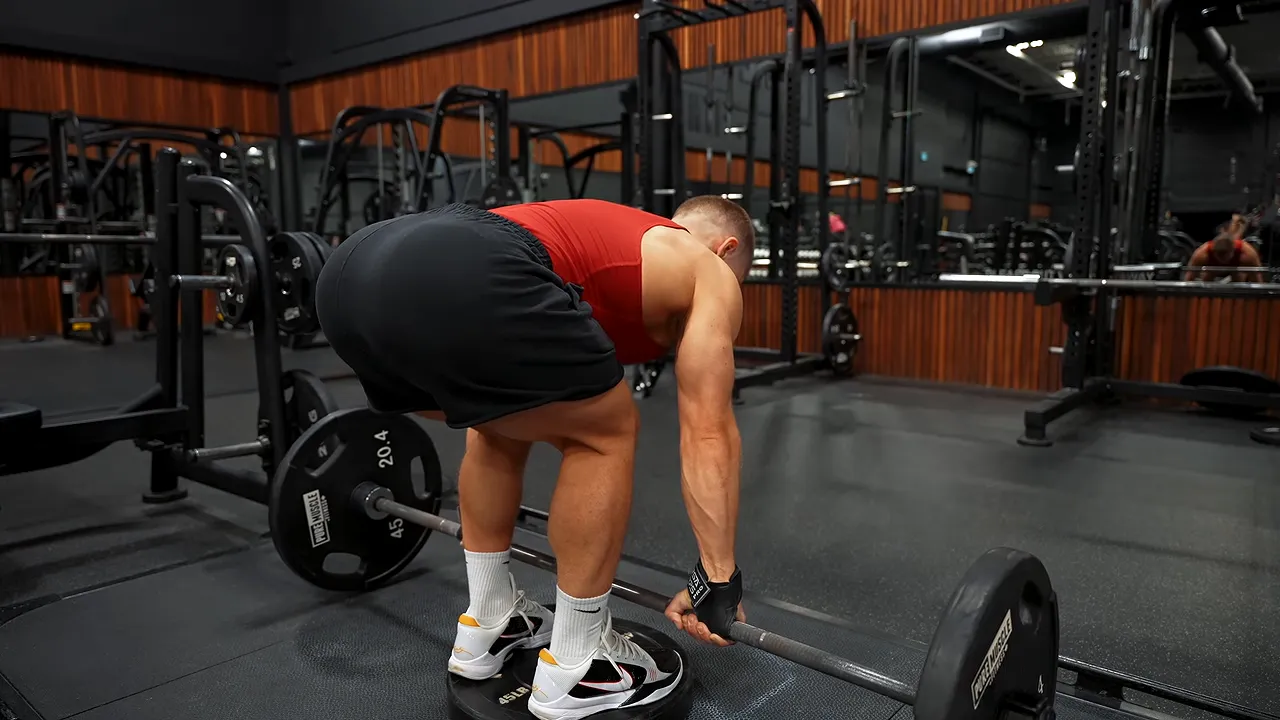 Side view of a bent-over barbell row while standing on a bumper plate
