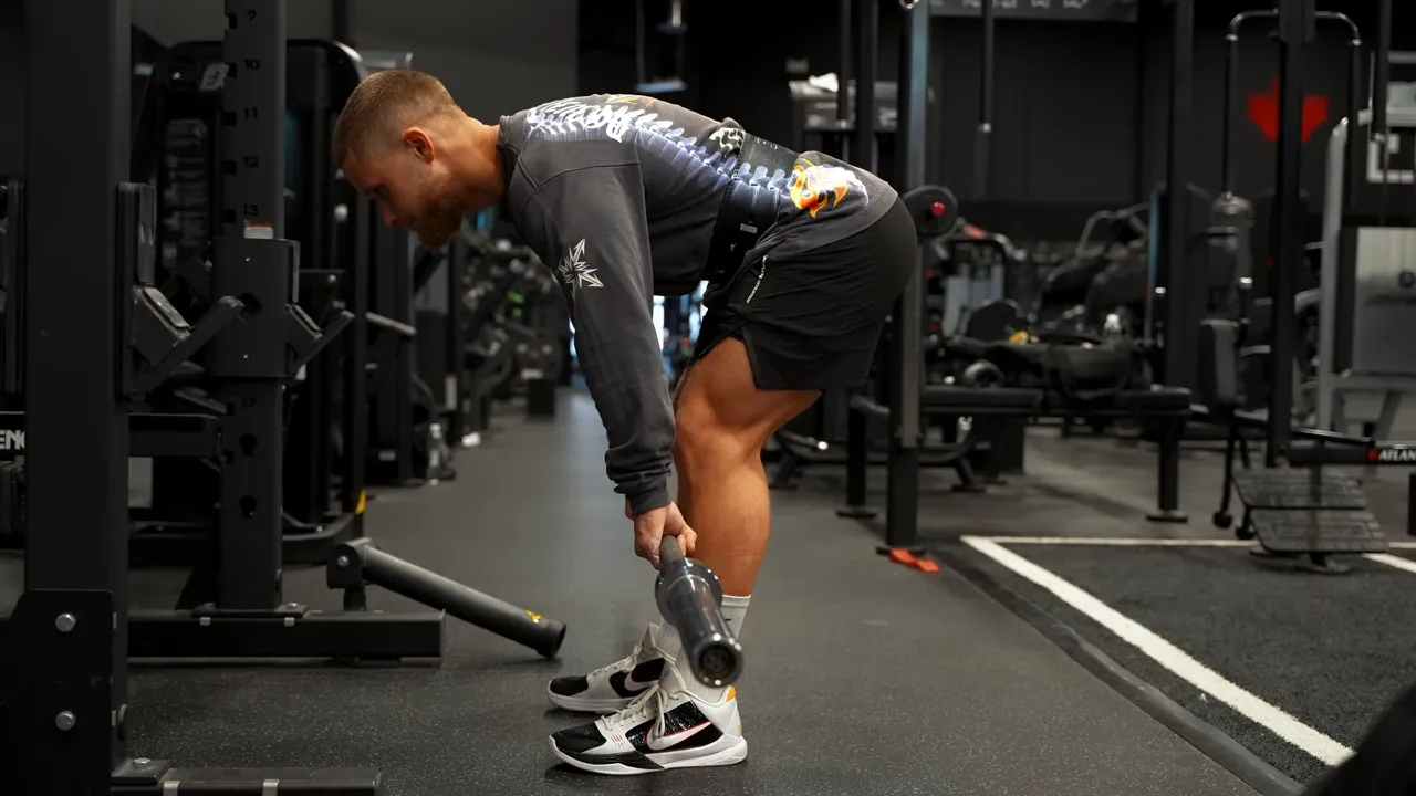 Side view of a Romanian deadlift with the hips pushed back, knees slightly bent, and the bar close to the legs