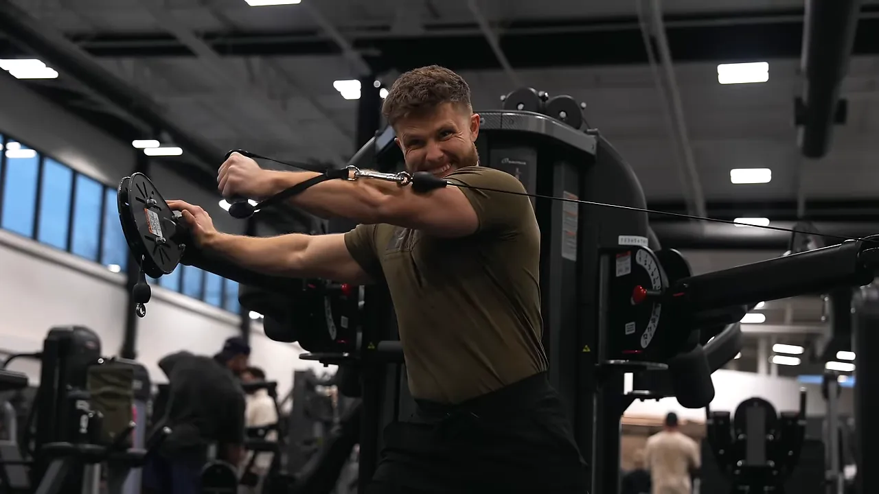 Lifter pressing a cable handle across his chest while holding a machine upright with the other hand
