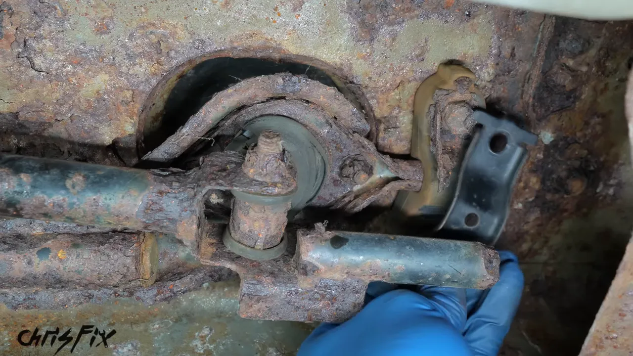 Replacement shifter bushing bracket held beside the rusted bracket under the car