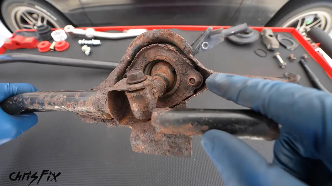 Heavily rusted shifter housing held beside a cleaner replacement linkage housing