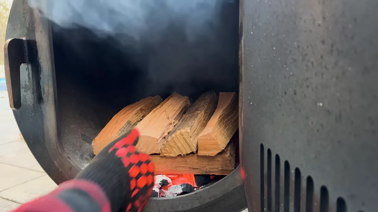 Wood splits stacked over glowing coals inside an open offset firebox
