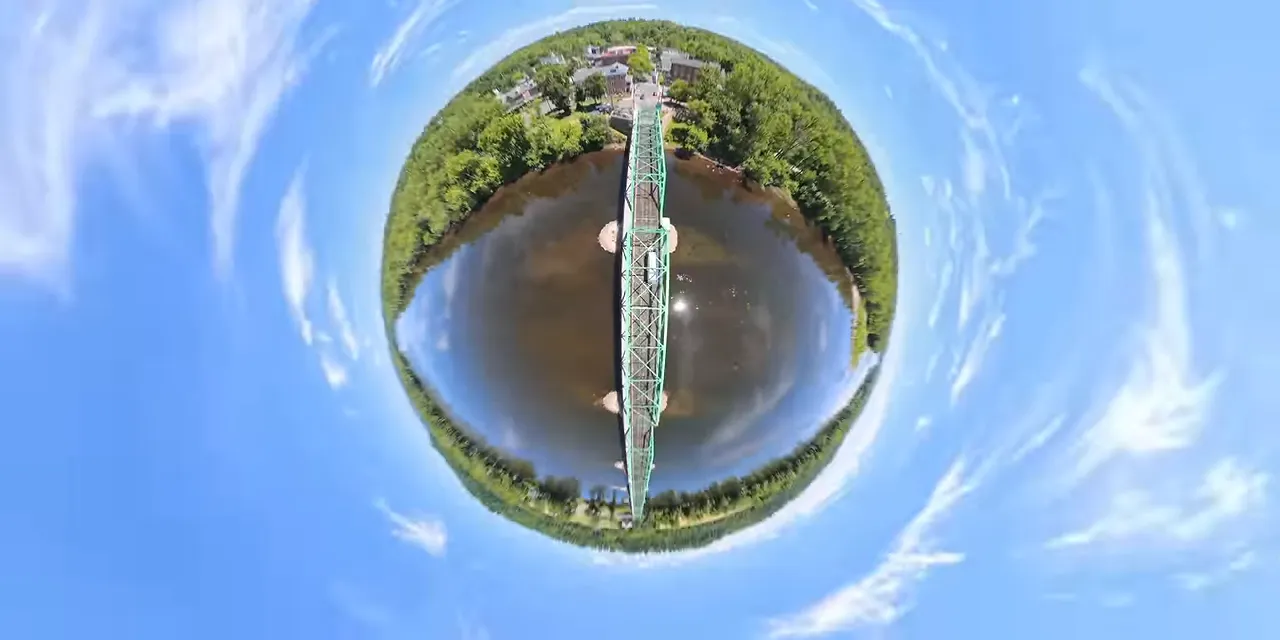 Tiny-planet perspective showing a green bridge and river wrapped into a globe against blue sky