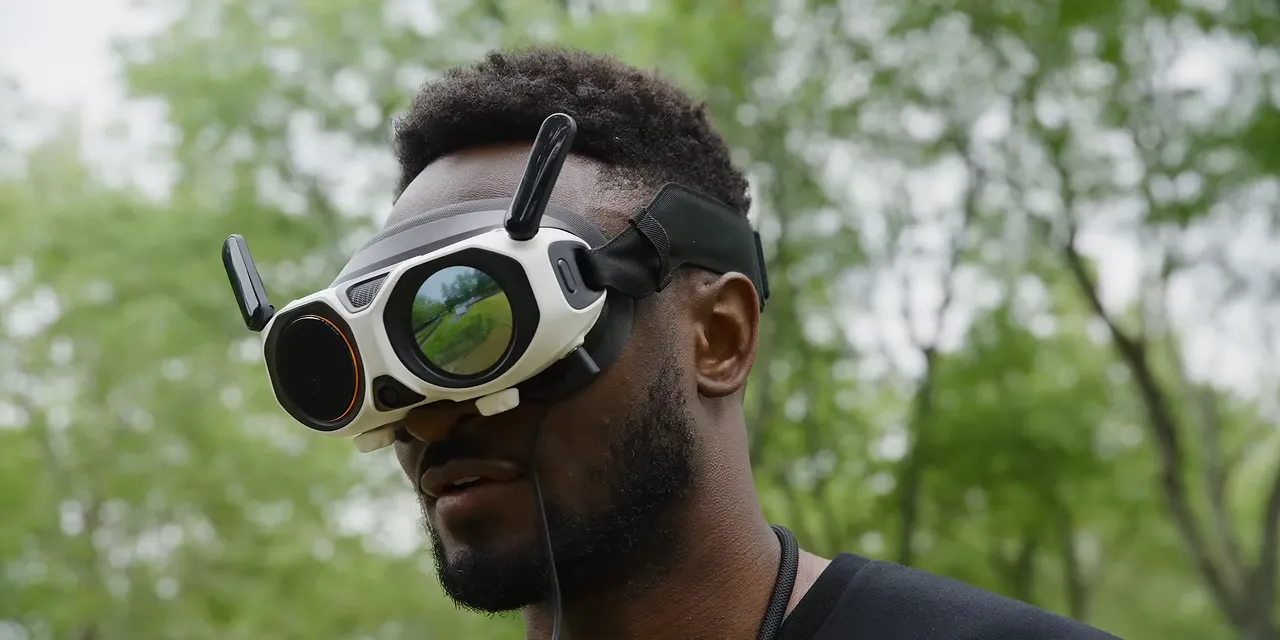Person wearing FPV goggles with an aerial image visible on the exterior display