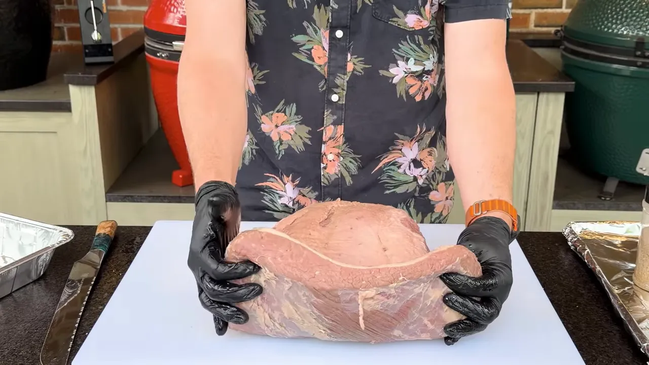 Gloved hands holding a raw brisket upright to show its thickness