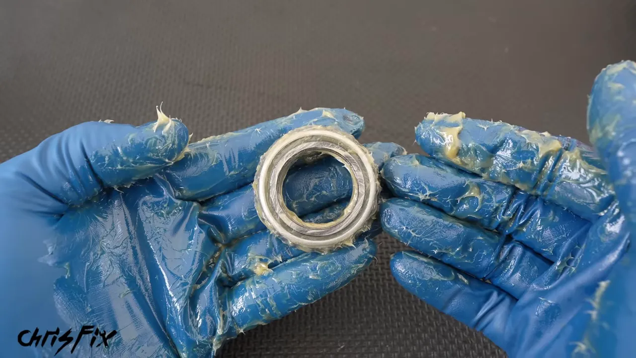 Packed tapered roller bearing held in grease-covered blue gloves