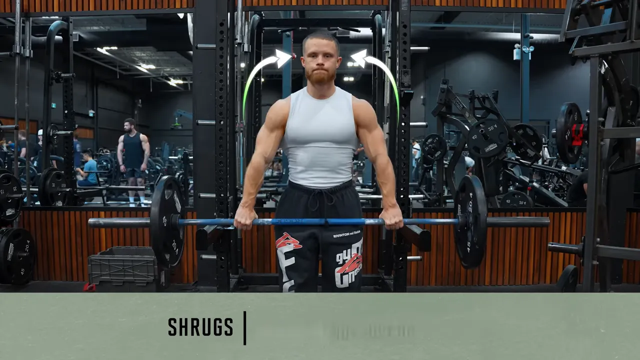 Jeff demonstrating a wide-grip barbell shrug with arrows curving upward and inward